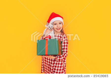 Girl holding kitten and gift against yellow background Girl holding kitten and gift against yellow background 85419065