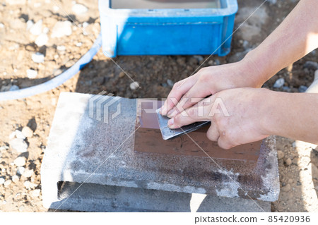 A carpenter who sharpens the blade of a plane with a whetstone 85420936