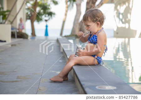 little girl eating ice cream yogurt with spoon sitting by outdoor pool little girl eating ice cream yogurt with spoon sitting by outdoor pool 85427786