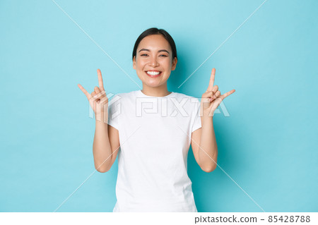 Carefree funny and upbeat pretty asian girl in white t-shirt, showing tongue and rock-n-roll gesture, enjoying awesome festival, looking pleased and amazed, partying over blue background Carefree funny and upbeat pretty asian girl in white t-shirt, showing tongue and rock-n-roll gesture, enjoying awesome festival, looking pleased and amazed, partying over blue background 85428788