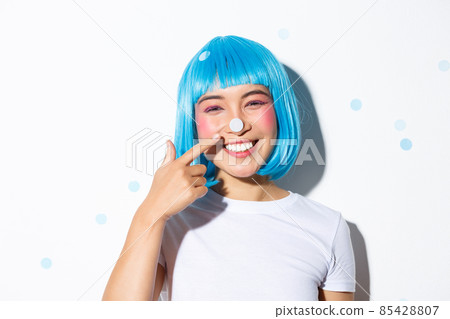 Image of cute and silly asian girl with confetti on her nose smiling and looking happy, wearing blue wig for halloween party Image of cute and silly asian girl with confetti on her nose smiling and looking happy, wearing blue wig for halloween party 85428807
