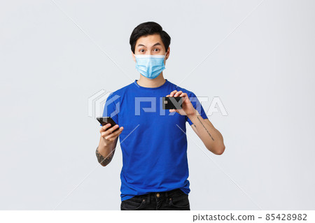 Contactless payment, online shopping during covid-19 and pandemic concept. Enthusiastic young man trying new bank feature, download application on smartphone, showing credit card 85428982