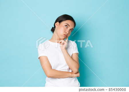 Bored or annoyed cute asian girl in white t-shirt roll eyes, lean on palm and looking indifferent, being not in mood, feeling boredom and apathy, standing blue background not concerned 85430008