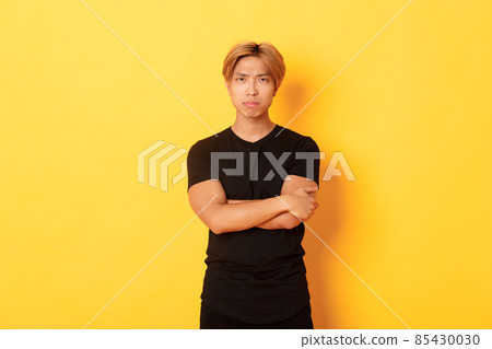 Worried serious-looking and concerned asian guy, cross arms chest and frowning at camera, yellow background 85430030