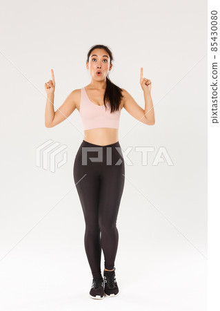 Full length of amazed and impressed asian female athelte, sportswoman in sportwear looking and pointing fingers up with excited face. Fitness girl wondered with special offer in sports store Full length of amazed and impressed asian female athelte, sportswoman in sportwear looking and pointing fingers up with excited face. Fitness girl wondered with special offer in sports store 85430080