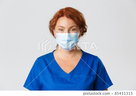 Medical workers, covid-19 pandemic, coronavirus concept. Close-up of middle-aged redhead female doctor, physician or vet in face mask and scrubs looking at camera, people working in hospital 85431315