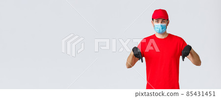 Covid-19, self-quarantine, online shopping and shipping concept. Excited delivery guy tell clients new promo, deliver bonuses or special prices, pointing fingers down, wear medical mask and gloves 85431451