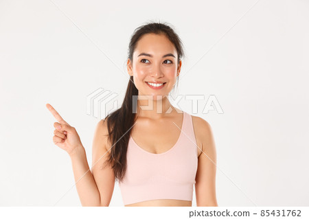Sport, wellbeing and active lifestyle concept. Close-up of smiling attractive asian fitness girl, female athlete picking new gear in store, pointing and looking upper left corner pleased 85431762
