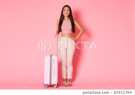 Travelling, holidays and vacation concept. Full-length of upbeat smiling asian girl in summer clothes standing ready for going abroad, holding suitcase over pink background 85431764