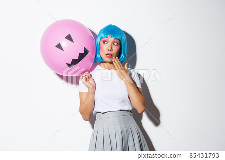 Cute and silly asian girl in blue wig, celebrating halloween, looking surprised at balloon with scary face Cute and silly asian girl in blue wig, celebrating halloween, looking surprised at balloon with scary face 85431793