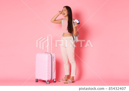 Travelling, holidays and vacation concept. Full-length of crying, sad and distressed asian girl tourist, feel depressed about missed flight, wiping tears, standing near suitcase over pink background 85432407