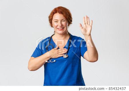 Medicine, healthcare and coronavirus concept. Smiling cute and optimistic middle-aged female doctor, nurse or medical worker in scrubs raise one hand and put palm on heart, swearing, making promise Medicine, healthcare and coronavirus concept. Smiling cute and optimistic middle-aged female doctor, nurse or medical worker in scrubs raise one hand and put palm on heart, swearing, making promise 85432437