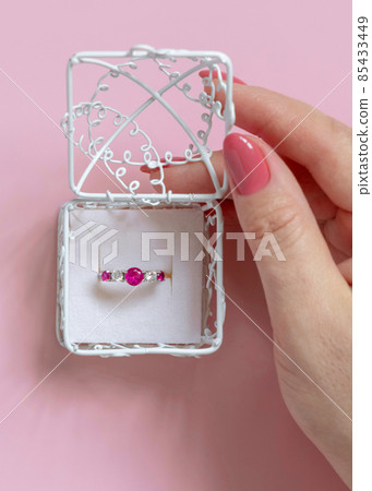 Womans hand opens a ornate gift box with a gemstone engatement ring on pink Womans hand opens a ornate gift box with a gemstone engatement ring on pink 85433449