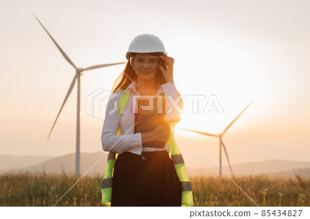 Woman in helmet posing at windmill farm with tablet in hands Woman in helmet posing at windmill farm with tablet in hands 85434827