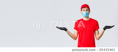 Groceries and packages delivery, covid-19, quarantine and shopping concept. Friendly delivery man in red uniform, face mask and gloves, holding two items or banners in hand, advice bonuses Groceries and packages delivery, covid-19, quarantine and shopping concept. Friendly delivery man in red uniform, face mask and gloves, holding two items or banners in hand, advice bonuses 85435461
