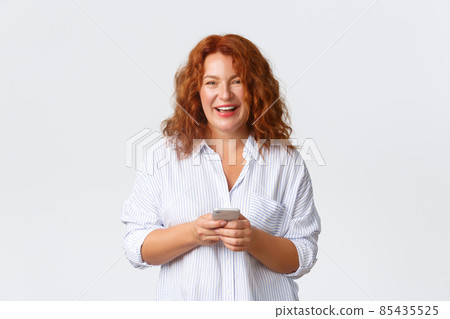 Portrait of mother, middle-aged redhead woman writing message, texting with smartphone. Wife looking at camera, holding mobile phone and smiling happy, using application over white background 85435525