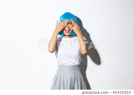 Excited beautiful asian girl peeking at camera amazed, looking at something interesting, dressed in blue wig and halloween costume, standing over white background Excited beautiful asian girl peeking at camera amazed, looking at something interesting, dressed in blue wig and halloween costume, standing over white background 85435833
