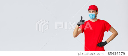 Covid-19, self-quarantine, online shopping and shipping concept. Friendly cheerful delivery guy in red uniform, gloves and face mask guarantee courier service quality, show thumb-up in like, approval 85436279