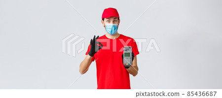 Contactless delivery, payment and online shopping during covid-19, self-quarantine. Excited courier in red uniform, face mask and gloves recommend pay order with POS terminal and credit card Contactless delivery, payment and online shopping during covid-19, self-quarantine. Excited courier in red uniform, face mask and gloves recommend pay order with POS terminal and credit card 85436687