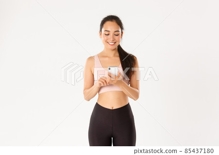 Sport, technology and active lifestyle concept. Smiling young female runner, healthy sportswoman using workout training app, water tracker or sports application on mobile phone, white background 85437180