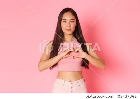 Lifestyle, beauty and women concept. Portrait of attractive smiling, happy asian girl confess in sympathy, like someone, showing heart gesture as feeling love, pink background Lifestyle, beauty and women concept. Portrait of attractive smiling, happy asian girl confess in sympathy, like someone, showing heart gesture as feeling love, pink background 85437362