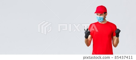 Contactless delivery, payment and online shopping during covid-19, self-quarantine. Enthusiastic courier in red uniform, face mask and gloves, rejoicing over good news, look smartphone screen 85437411