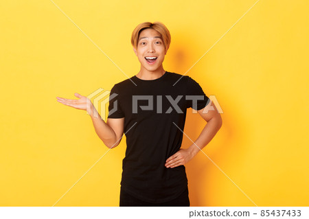 Portrait of happy and excited smiling asian guy holding something on hand over yellow background 85437433