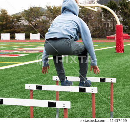 High school bly jumping over hurdle on a turf field High school bly jumping over hurdle on a turf field 85437469