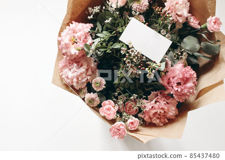 Floral wedding, birthday mockup. Blank business card, invitatio. Pink floral bouquet in craft paper isolated on white table background. Eustoma, santini mums and carnations with ucalyptus. Top view. Floral wedding, birthday mockup. Blank business card, invitatio. Pink floral bouquet in craft paper isolated on white table background. Eustoma, santini mums and carnations with ucalyptus. Top view. 85437480