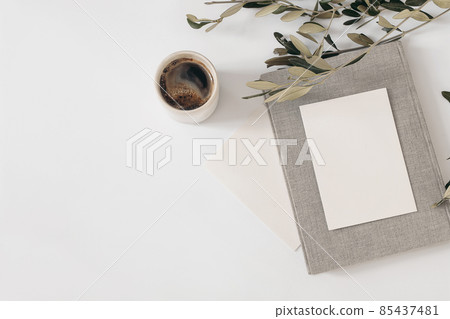 Summer still life. Cup of coffee, blank greeting card mockups with vintage book. Olive tree branch isolated on white table background. Mediterranean wedding stationery. Flat lay, top view. Breakfast 85437481