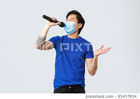 Covid-19 lifestyle, people emotions and leisure on quarantine concept. Handsome funny young male student staying home during coronavirus pandemic, wear mask and singing karaoke in microphone Covid-19 lifestyle, people emotions and leisure on quarantine concept. Handsome funny young male student staying home during coronavirus pandemic, wear mask and singing karaoke in microphone 85437654