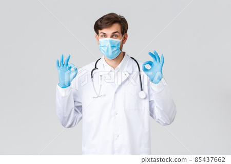 Hospital, healthcare workers, covid-19 treatment concept. Take it easy, all good. Doctor in medical mask, white scrubs and gloves, showing okay sign, approve and recommend medical treatment 85437662