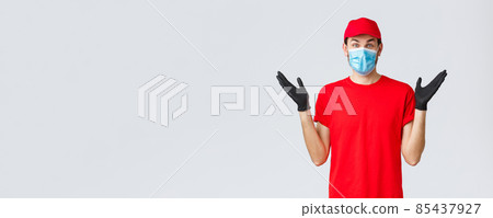 Groceries and packages delivery, covid-19, quarantine and shopping concept. Happy rejoicing delivery guy in red uniform, face mask and gloves receive good news, clap hands applause surprised 85437927
