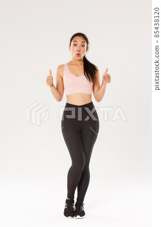 Full length of amazed and impressed female athlete in activewear, showing thumbs-up in approval and looking wondered, praise great workout program, fitness training app or gym membership prices 85438120