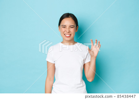 Sassy and funny, cute asian girl in white t-shirt showing paws gesture and making roar as if imitating cat playfully, standing flirty over blue background, sending coquettish vibes 85438447