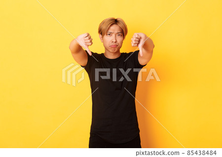 Portrait of disappointed and upset asian man showing thumbs-down, grimacing displeased, yellow background Portrait of disappointed and upset asian man showing thumbs-down, grimacing displeased, yellow background 85438484