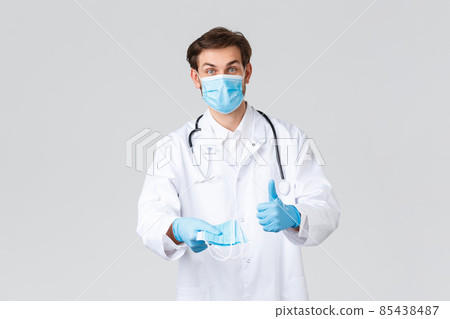 Hospital, healthcare workers, covid-19 treatment concept. Cheerful doctor in scrubs, protective equipment during coronavirus, explaining necessity of wearing medical masks, show thumb-up Hospital, healthcare workers, covid-19 treatment concept. Cheerful doctor in scrubs, protective equipment during coronavirus, explaining necessity of wearing medical masks, show thumb-up 85438487