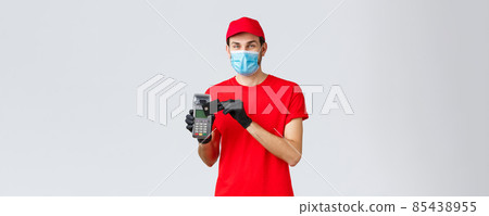 Contactless delivery, payment and online shopping during covid-19, self-quarantine. Friendly courier in red uniform, gloves and face mask, showing paying order with POS terminal and credit card Contactless delivery, payment and online shopping during covid-19, self-quarantine. Friendly courier in red uniform, gloves and face mask, showing paying order with POS terminal and credit card 85438955