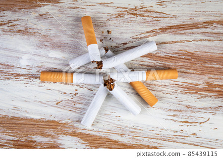 Stack of broken cigarettes on a white painted wooden background 85439115