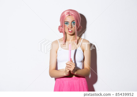 Image of annoyed girl in pink wig, holding candle and showing teeth, celebrating halloween, standing over white background 85439952