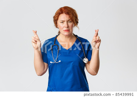 Medicine, healthcare and coronavirus concept. Nervous and hopeful middle-aged medical worker, female doctor praying or making wish, hoping with fingers crossed, standing grey background pleading 85439991