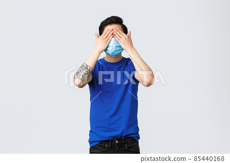 Different emotions, social distancing, self-quarantine on covid-19 and lifestyle concept. Asian man in blue t-shirt and medical mask standing blindfolded, cover eyes not see what happening 85440168