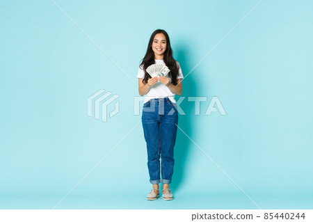 Fashion, beauty and lifestyle concept. Full-length of smiling young asian woman showing dollars, earn money and looking satisfied, winning lottery, standing with cash over light blue background 85440244