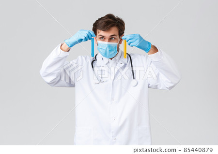 Hospital, healthcare workers, covid-19 treatment concept. Professional lab technician in white scrubs, medical mask and gloves, studying samples, searching vaccine, look ampoule Hospital, healthcare workers, covid-19 treatment concept. Professional lab technician in white scrubs, medical mask and gloves, studying samples, searching vaccine, look ampoule 85440879