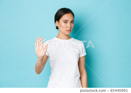 Serious-looking displeased asian girl looking reluctant and bothered, raise hand in stop gesture and looking annoyed, disapprove something, refuse or disagree, standing blue background 85440991