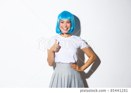 Portrait of happy asian girl in blue wig, showing thumbs-up in approval, recommend something, standing over white background 85441281
