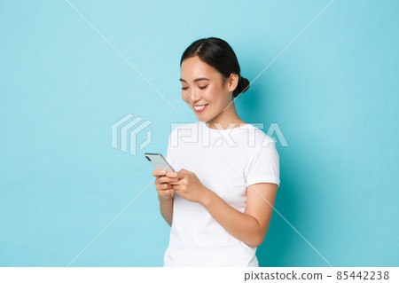 Lifestyle, technology and e-commerce concept. Side view of attractive asian girl using mobile phone, texting, messaging or chatting with friends online, looking at smartphone screen pleased Lifestyle, technology and e-commerce concept. Side view of attractive asian girl using mobile phone, texting, messaging or chatting with friends online, looking at smartphone screen pleased 85442238