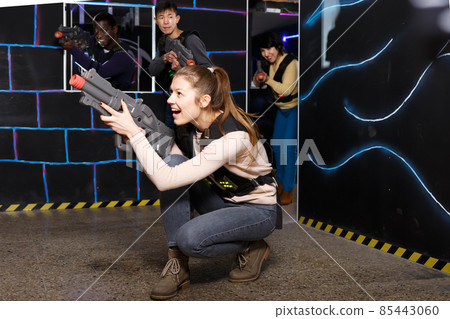 Happy girl aiming laser gun during lasertag game Happy girl aiming laser gun during lasertag game 85443060