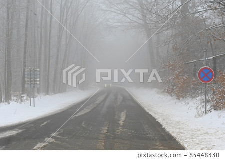 Bad weather driving - foggy hazy country road. Motorway - road traffic. Winter time and snow. 85448330