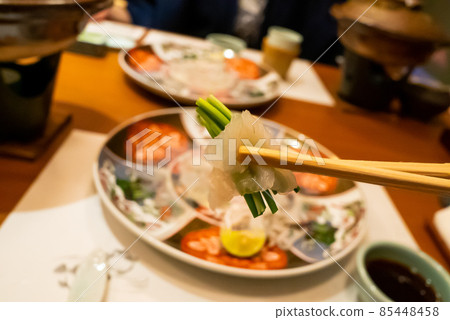 Show the blowfish sashimi wrapped with green onions with chopsticks Show the blowfish sashimi wrapped with green onions with chopsticks 85448458